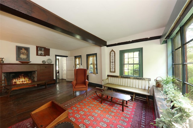 living room featuring hardwood / wood-style flooring, a warm lit fireplace, and beamed ceiling