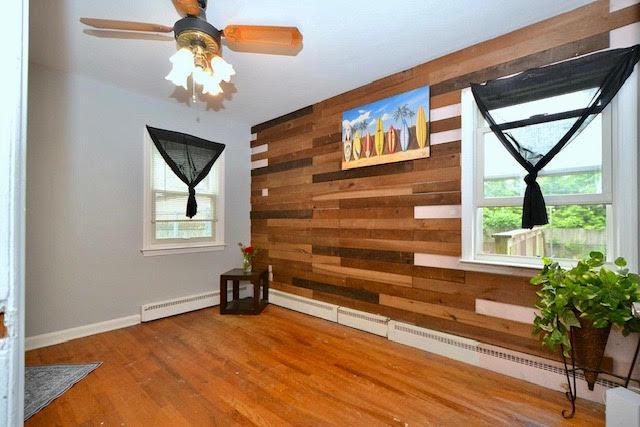 70 Islip Ave, Islip, NY 11751 - empty room featuring wooden walls, a baseboard radiator, wood finished floors, and a ceiling fan
