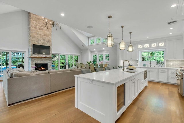 120 Cambon Ave, Saint James, NY 11780 - kitchen featuring white cabinetry, light wood-style floors, backsplash, a stone fireplace, and open floor plan