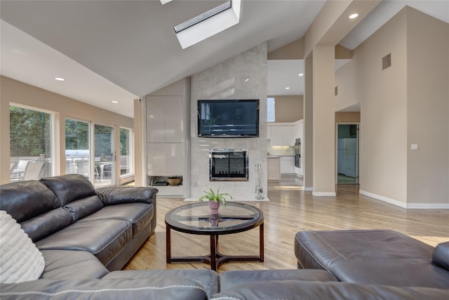 64 Highland Ave, Roslyn, NY 11576 - living room with high vaulted ceiling, a tiled fireplace, a skylight, light wood-type flooring, and recessed lighting