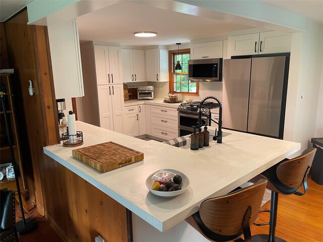 1289 State Route 208, Wallkill, NY 12589 - kitchen with appliances with stainless steel finishes, white cabinetry, light countertops, wood finished floors, and a kitchen breakfast bar