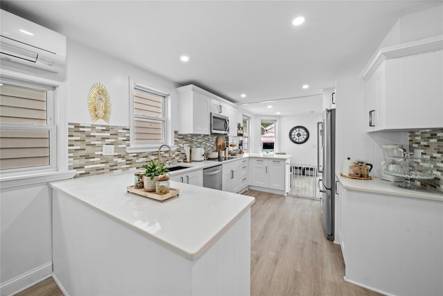 3234 204th St, Bayside, NY 11361 - kitchen with appliances with stainless steel finishes, a wall unit AC, a peninsula, light wood-style floors, and decorative backsplash