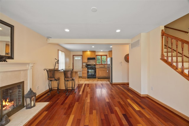 65 Netherwood Dr, Albertson, NY 11507 - kitchen featuring black range with gas cooktop, wood-type flooring, a tiled fireplace, freestanding refrigerator, and under cabinet range hood