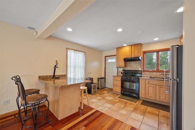 65 Netherwood Dr, Albertson, NY 11507 - kitchen with gas stove, under cabinet range hood, freestanding refrigerator, a breakfast bar area, and a peninsula