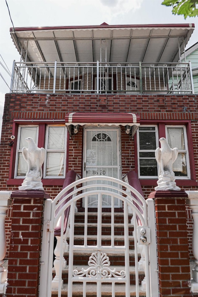 8620 130th St, Richmond Hill, NY 11418 - view of exterior entry with brick siding, a gate, a balcony, and a security system