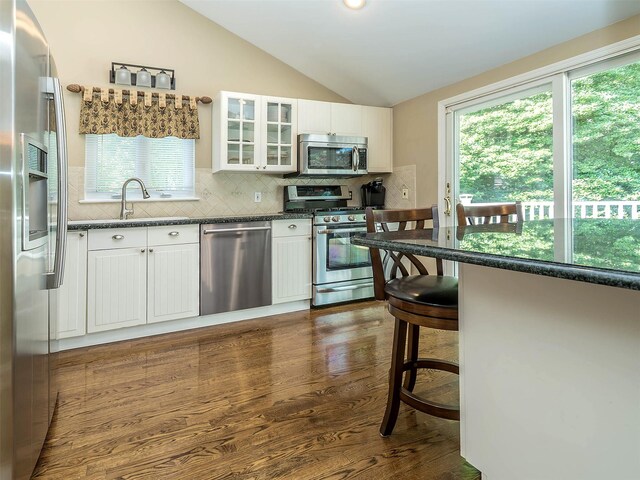 1 Barry Dr, Glen Cove, NY 11542 - kitchen with appliances with stainless steel finishes, vaulted ceiling, white cabinets, backsplash, and glass insert cabinets