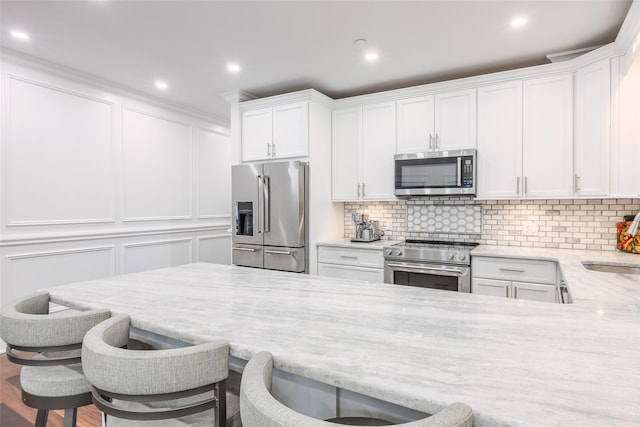 114 Atlantic Ave Unit 82, Lynbrook, NY 11563 - kitchen featuring high end appliances, a breakfast bar, a decorative wall, white cabinetry, and light stone countertops