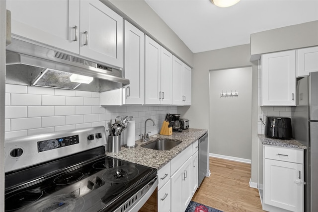129 Main St Unit D12, Cornwall, NY 12518 - kitchen with stainless steel appliances, under cabinet range hood, white cabinetry, light stone countertops, and backsplash