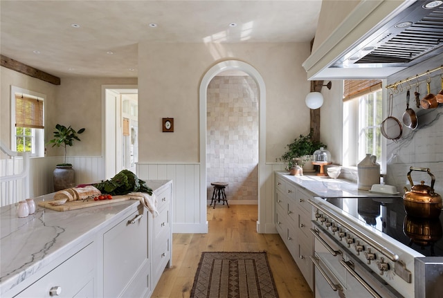 1174 Potter Mountain Rd, Gilboa, NY 12076 - kitchen with ventilation hood, a wainscoted wall, light wood finished floors, white cabinets, and light stone countertops