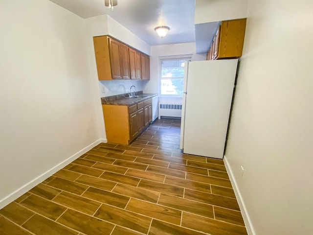 1365 Crosby Ave, Bronx, NY 10461 - kitchen with freestanding refrigerator, radiator heating unit, wood tiled floors, brown cabinetry, and dark countertops