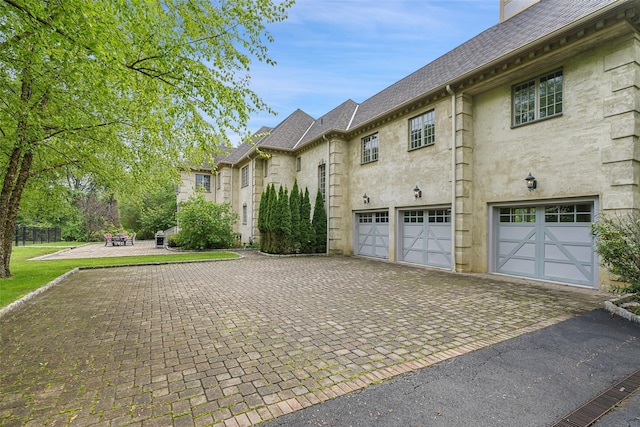 3747 Purchase St, Purchase, NY 10577 - view of side of home with decorative driveway, a garage, a shingled roof, a chimney, and a fire pit