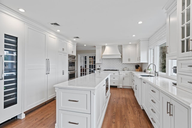 8 Pippin Ln, Lloyd Harbor, NY 11743 - kitchen with custom range hood, double oven, white cabinetry, wood finished floors, and a center island