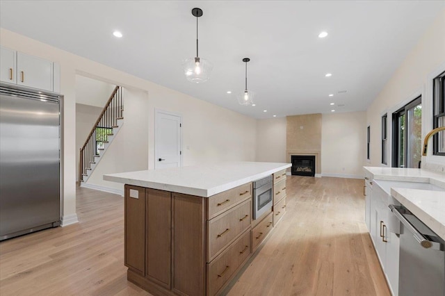 4 Haven Ln, Old Bethpage, NY 11804 - kitchen featuring built in appliances, light wood finished floors, light countertops, decorative light fixtures, and a fireplace