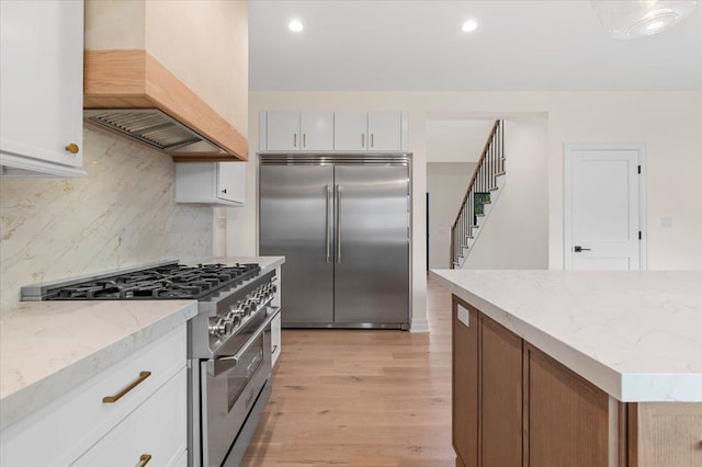 4 Haven Ln, Old Bethpage, NY 11804 - kitchen with high end appliances, custom range hood, decorative backsplash, light wood-style flooring, and light stone countertops