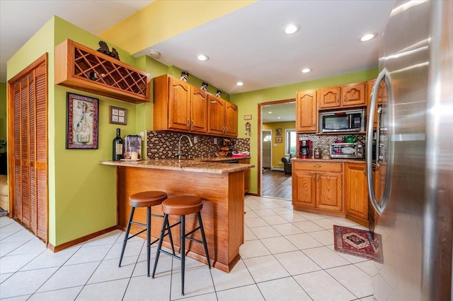 686 Barnes Ave, Baldwin, NY 11510 - kitchen featuring appliances with stainless steel finishes, a peninsula, tasteful backsplash, a kitchen bar, and light tile patterned floors