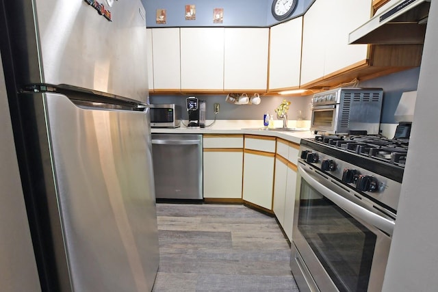 310 Fairview Cir, Middle Island, NY 11953 - kitchen featuring stainless steel appliances, under cabinet range hood, light countertops, light wood-style flooring, and white cabinets