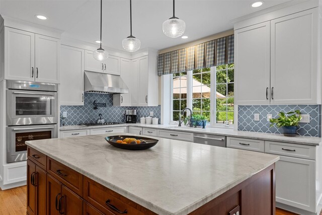 41 Carlton Dr, Mount Kisco, NY 10549 - kitchen featuring stainless steel appliances, under cabinet range hood, a kitchen island, decorative backsplash, and white cabinetry