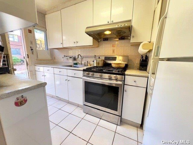 220-34 67th Ave Duplex, Unit Duplex, Bayside, NY 11364 - kitchen featuring freestanding refrigerator, stainless steel gas range oven, under cabinet range hood, light countertops, and backsplash