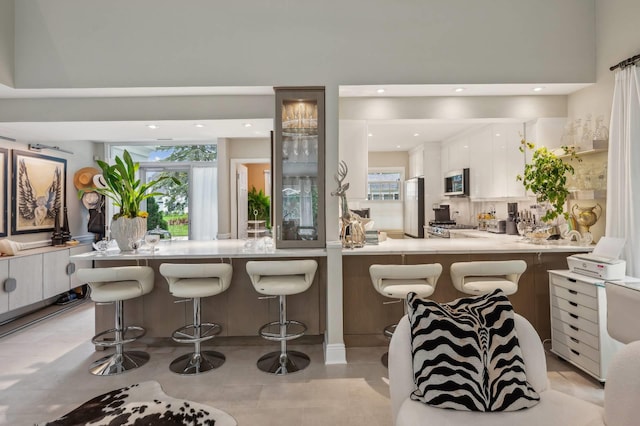 545 Hampton Rd Unit 16, Southampton, NY 11968 - kitchen featuring appliances with stainless steel finishes, a peninsula, white cabinetry, a kitchen breakfast bar, and light countertops
