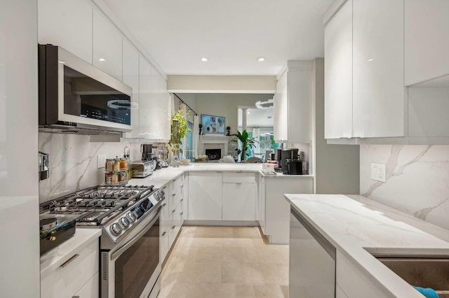 545 Hampton Rd Unit 16, Southampton, NY 11968 - kitchen with appliances with stainless steel finishes, modern cabinets, decorative backsplash, white cabinets, and light stone counters