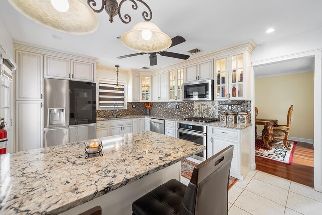427 Benito St, East Meadow, NY 11554 - kitchen featuring appliances with stainless steel finishes, light stone countertops, light tile patterned floors, a breakfast bar area, and backsplash