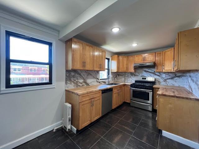 4118 Hill Ave, Bronx, NY 10466 - kitchen featuring appliances with stainless steel finishes, under cabinet range hood, radiator, tasteful backsplash, and recessed lighting