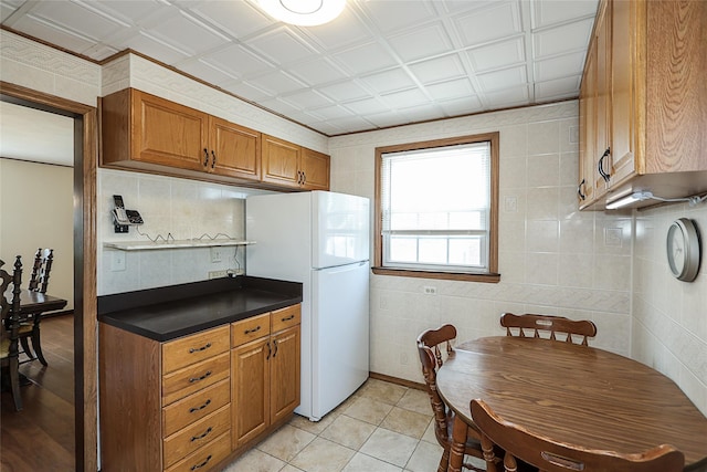 2199 Mcarthur St, East Meadow, NY 11554 - kitchen featuring freestanding refrigerator, dark countertops, brown cabinetry, light tile patterned floors, and tasteful backsplash