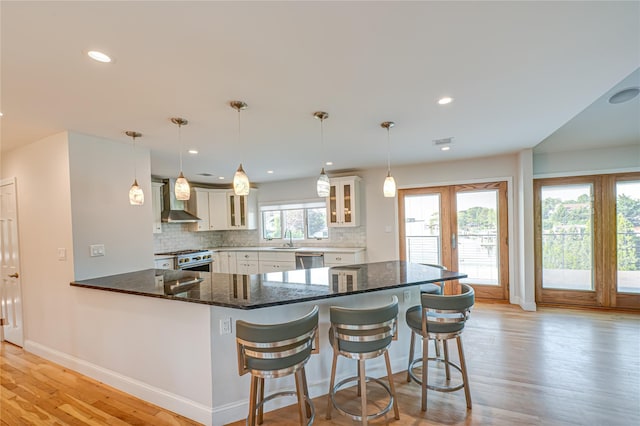 714 Montauk, West Islip, NY 11795 - kitchen featuring wall chimney exhaust hood, stainless steel appliances, light wood-style flooring, a peninsula, and tasteful backsplash