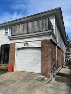 214-05 23rd Ave, Bayside, NY 11360 - view of side of property with an attached garage, a balcony, brick siding, and driveway
