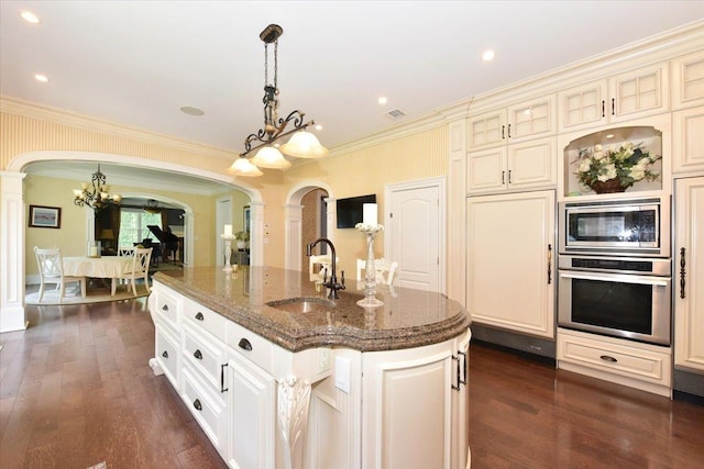 1616 Stewart Ln, Laurel Hollow, NY 11791 - kitchen with stainless steel appliances, cream cabinetry, a chandelier, arched walkways, and decorative columns