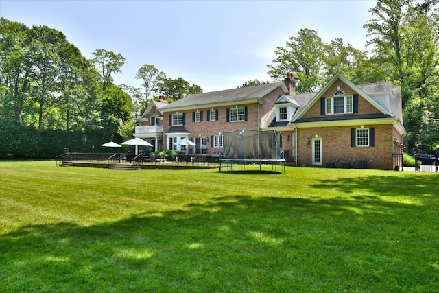 1616 Stewart Ln, Laurel Hollow, NY 11791 - rear view of property with a trampoline, a lawn, brick siding, and a wooden deck