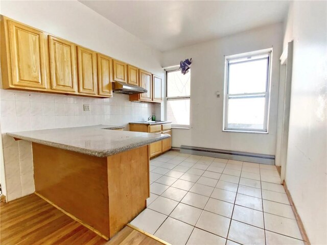1363 64th St, Brooklyn, NY 11219 - kitchen with under cabinet range hood, a peninsula, a baseboard radiator, tasteful backsplash, and light stone countertops