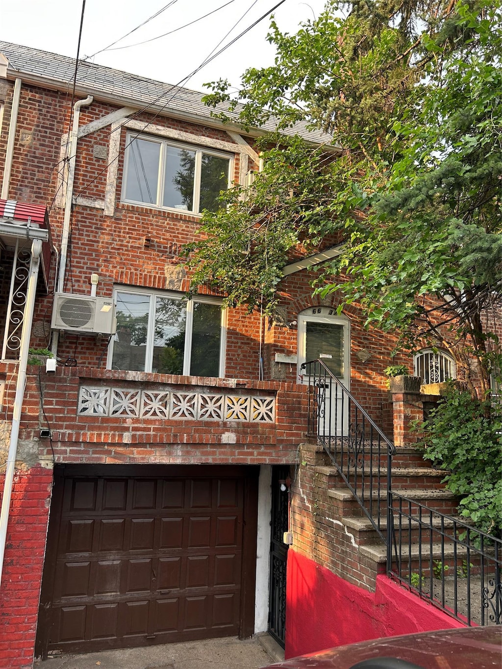 66-37 Burns St, Rego Park, NY 11374 - view of front of house with brick siding, a garage, and an AC wall unit