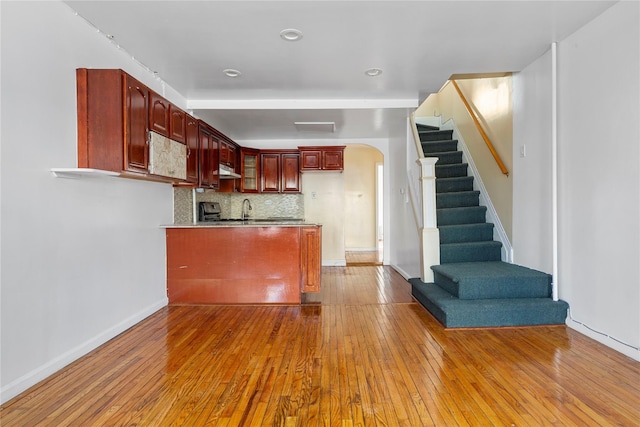 117-66 127th St, South Ozone Park, NY 11420 - kitchen with reddish brown cabinets, arched walkways, a peninsula, hardwood / wood-style floors, and under cabinet range hood