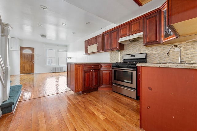 117-66 127th St, South Ozone Park, NY 11420 - kitchen featuring stainless steel gas stove, under cabinet range hood, light wood-style flooring, radiator heating unit, and tasteful backsplash