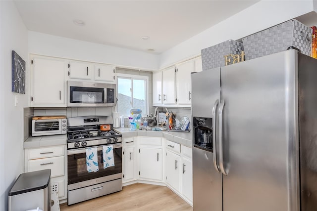 556 Long Beach Rd, Island Park, NY 11558 - kitchen featuring appliances with stainless steel finishes, white cabinets, backsplash, tile counters, and light wood-style floors