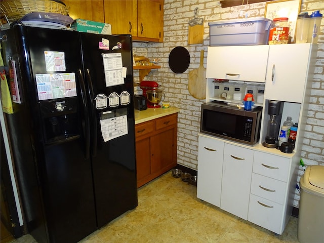 524 Polaris St, North Babylon, NY 11703 - kitchen featuring black fridge, stainless steel microwave, brick wall, light countertops, and white cabinetry
