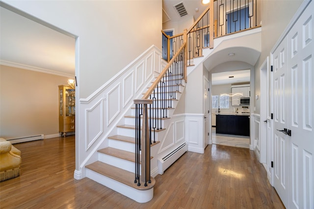83 N Airmont Rd, Suffern, NY 10901 - stairs with a baseboard heating unit, wood finished floors, ornamental molding, a high ceiling, and arched walkways