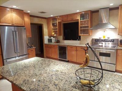 404 Club Ct, Oceanside, NY 11572 - kitchen featuring appliances with stainless steel finishes, wall chimney exhaust hood, wine cooler, recessed lighting, and glass insert cabinets