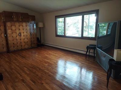 404 Club Ct, Oceanside, NY 11572 - unfurnished living room with a baseboard radiator, wood finished floors, and lofted ceiling