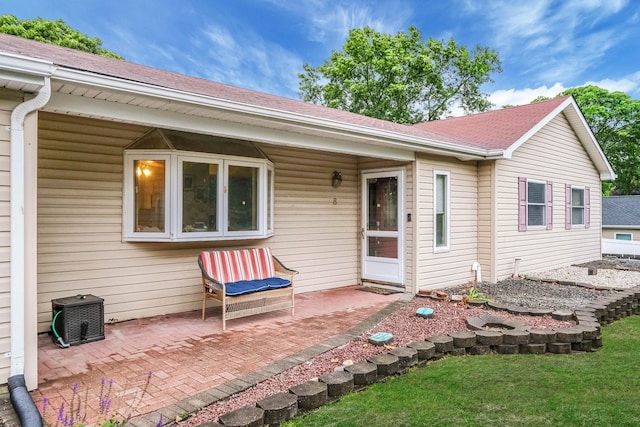 8 Peconic Ln, Selden, NY 11784 - view of exterior entry featuring a patio area, a shingled roof, and a lawn