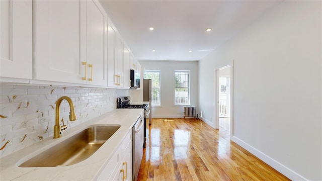 442 Newport St, Brooklyn, NY 11207 - kitchen with radiator, tasteful backsplash, stainless steel appliances, white cabinets, and light wood-style floors