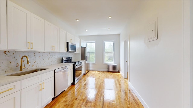 442 Newport St, Brooklyn, NY 11207 - kitchen with stainless steel appliances, radiator, backsplash, light wood finished floors, and white cabinets