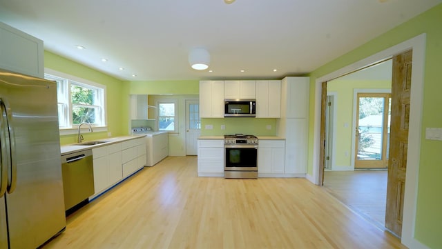 412 Atlantic Ave, Greenport, NY 11944 - kitchen with appliances with stainless steel finishes, washing machine and clothes dryer, light wood-style floors, white cabinets, and light countertops