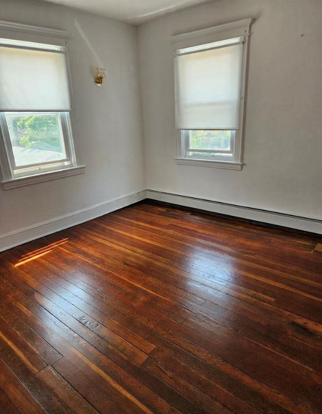 1430 Gipson St, Far Rockaway, NY 11691 - unfurnished room featuring healthy amount of natural light, a baseboard heating unit, and wood-type flooring