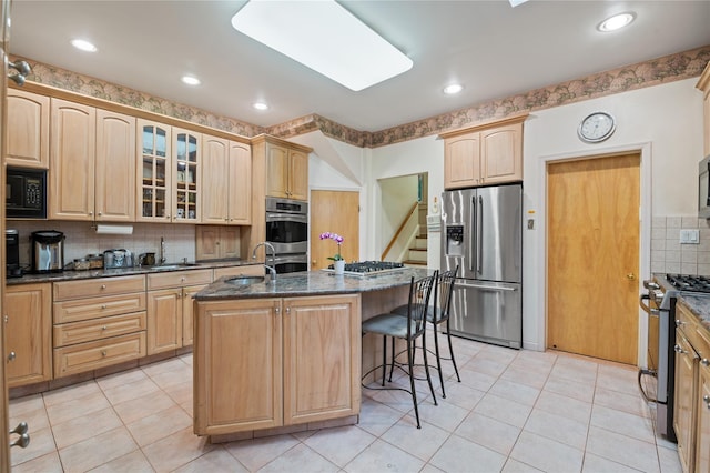 1020 New Mcneil Ave, Lawrence, NY 11559 - kitchen with stainless steel appliances, light brown cabinets, a breakfast bar area, glass insert cabinets, and dark stone countertops