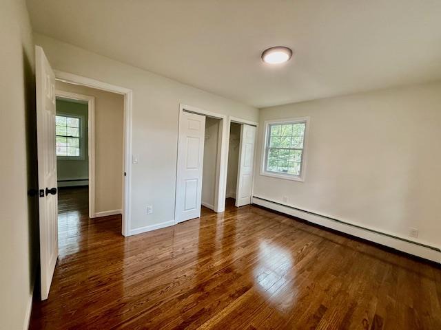 30 7th St, Holbrook, NY 11741 - unfurnished bedroom featuring a baseboard radiator, wood finished floors, two closets, and a baseboard heating unit