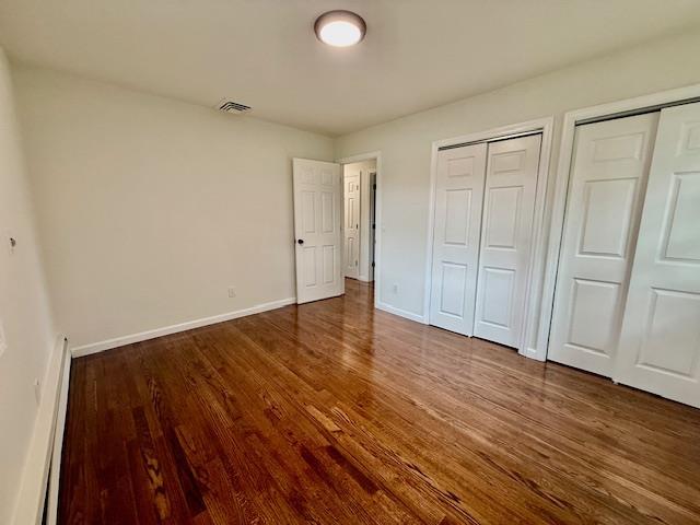30 7th St, Holbrook, NY 11741 - unfurnished bedroom featuring a baseboard radiator, multiple closets, and wood finished floors