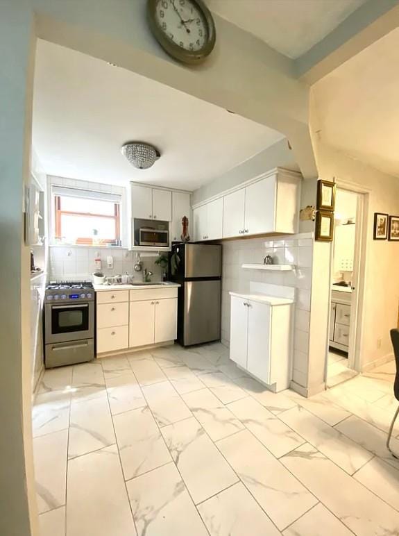 22-39 74th St, East Elmhurst, NY 11370 - kitchen with stainless steel appliances, light countertops, light marble finish floors, white cabinetry, and tasteful backsplash