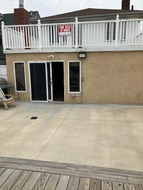 16330 95th St, Howard Beach, NY 11414 - rear view of house featuring a balcony, a chimney, a patio area, and stucco siding